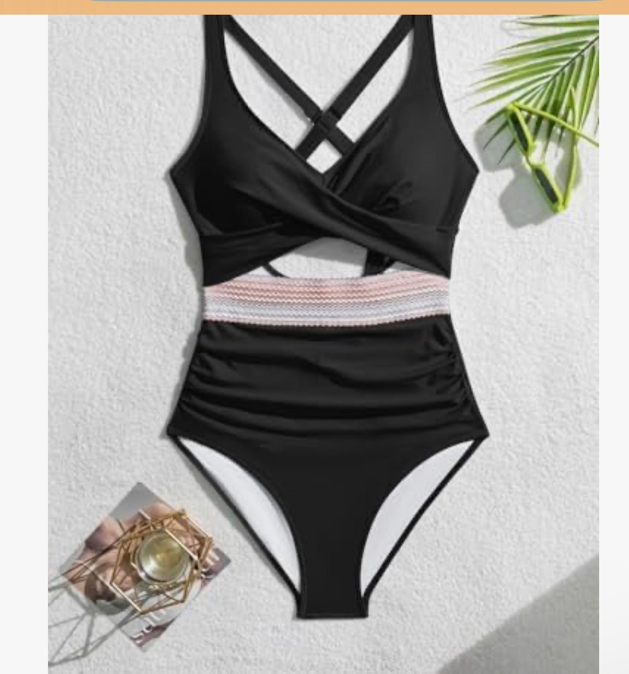 Black swimsuit with criss-cross straps on a textured white surface.