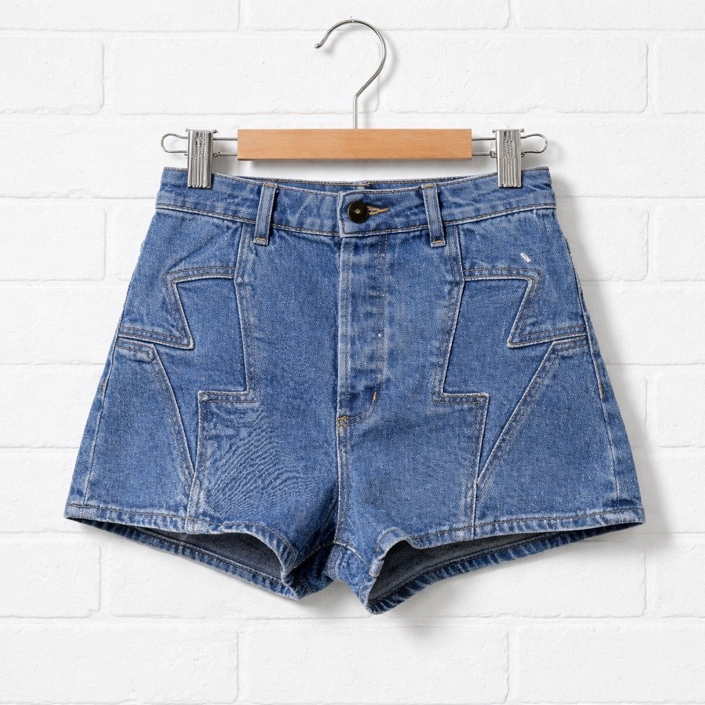 Blue denim shorts on a hanger against a white brick wall.