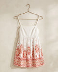 White dress with red floral patterns on a hanger against a beige wall