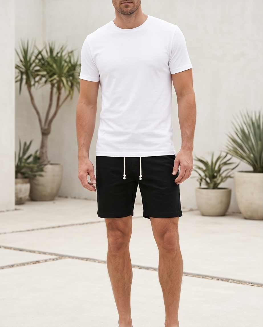 Man wearing a white t-shirt and black shorts standing in front of a white wall with plants.