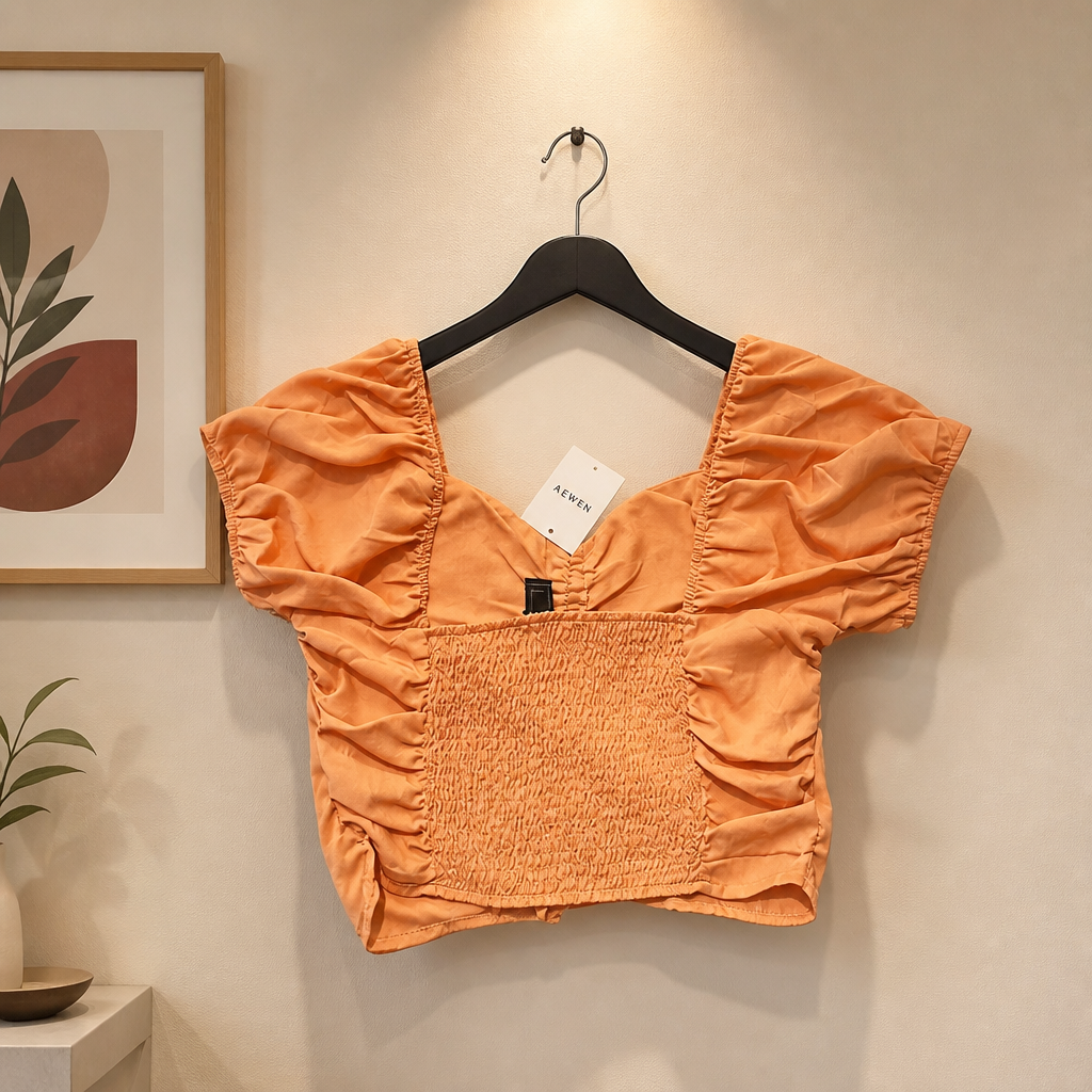 Orange crop top on a hanger against a beige wall with a plant and framed picture.