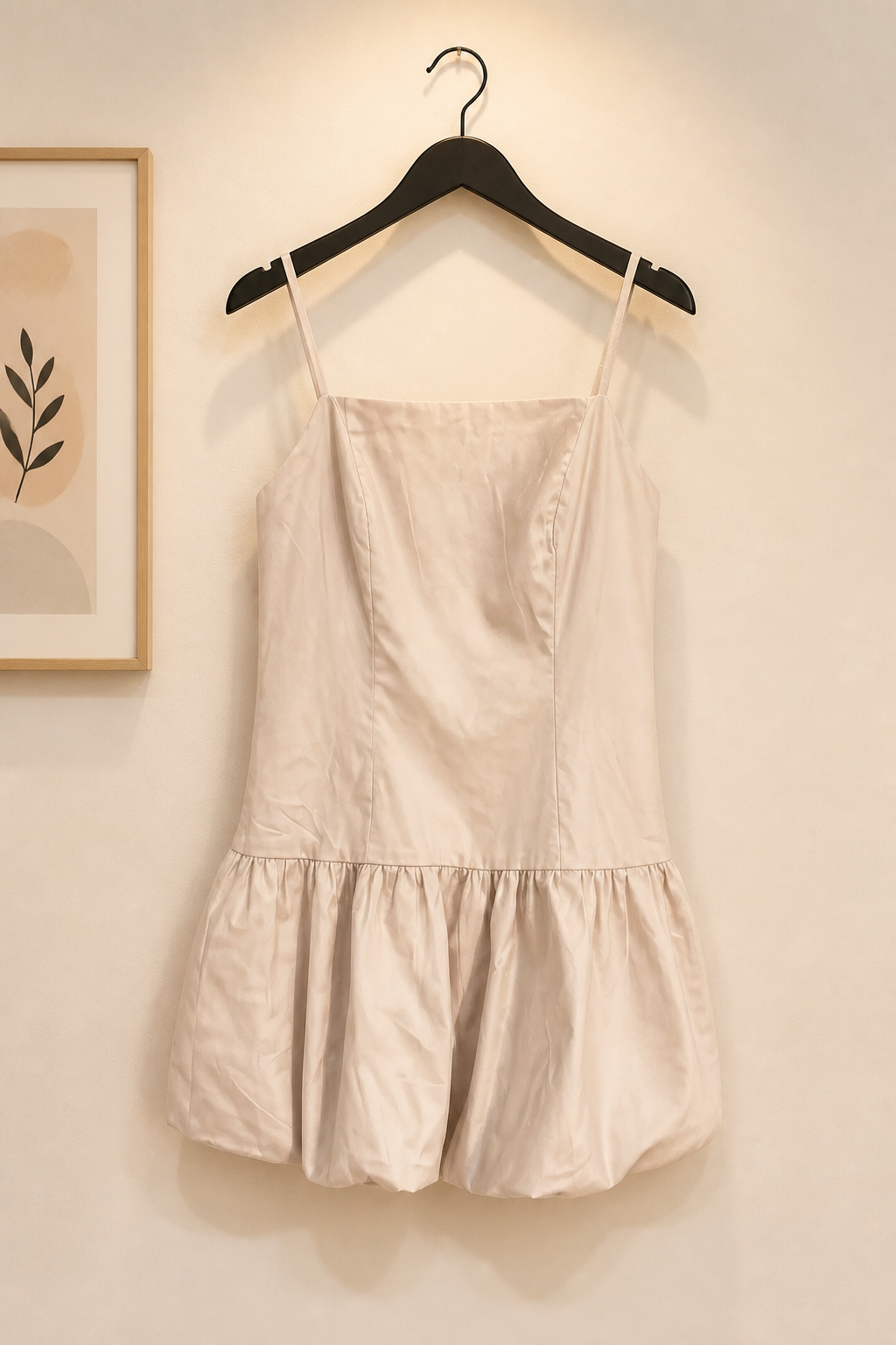 Beige dress hanging on a hanger against a neutral wall.