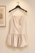 Beige dress hanging on a hanger against a neutral wall.