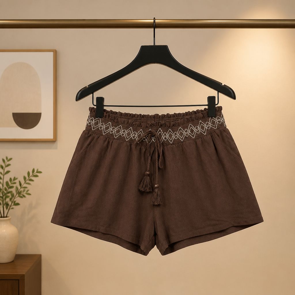 Brown shorts with decorative waistband on a hanger against a neutral wall.