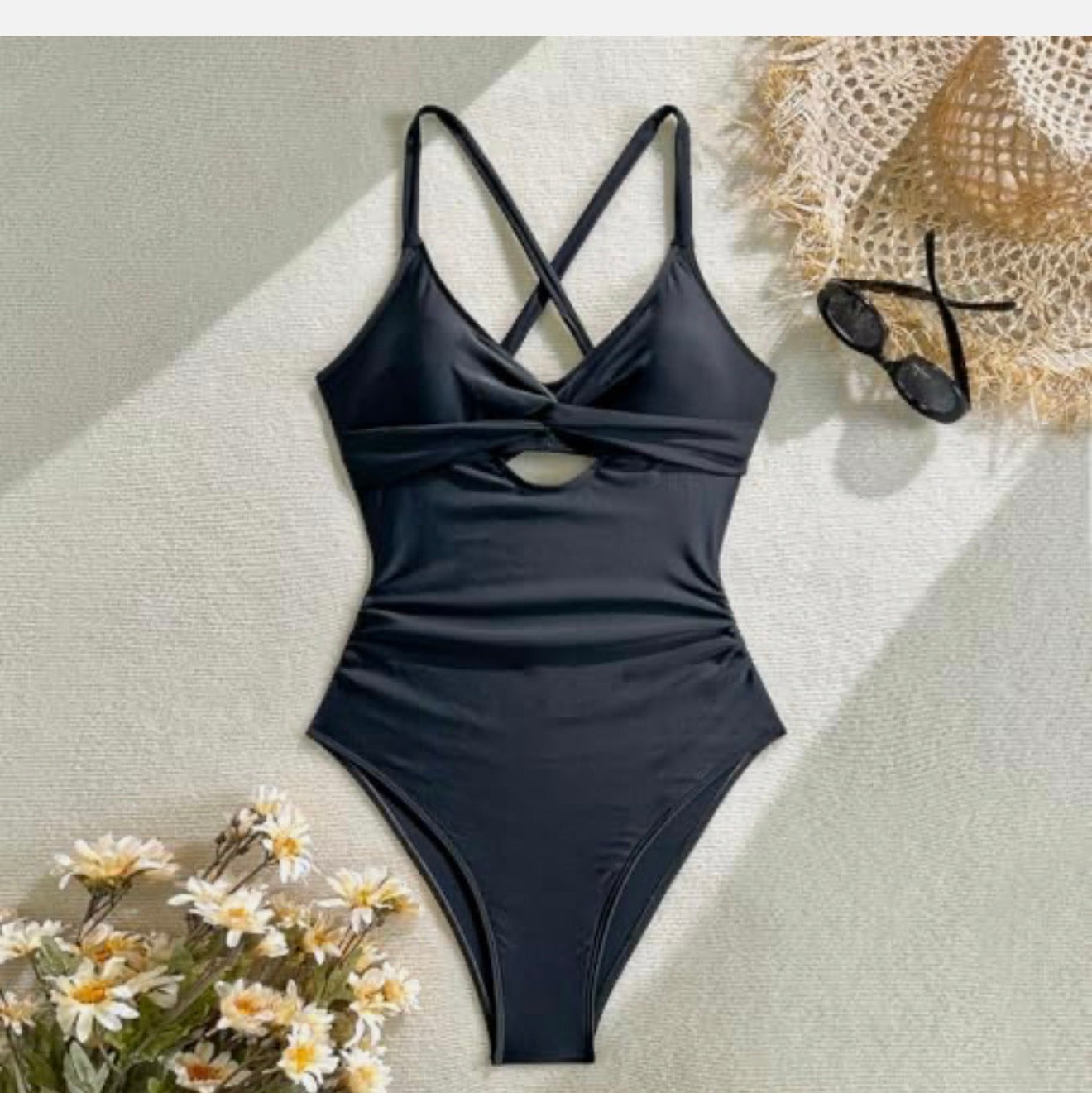 Black swimsuit on a light surface with flowers and sunglasses