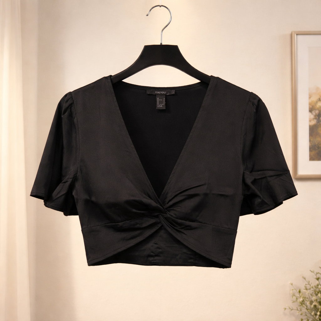 Black crop top with a knot detail on a hanger against a neutral wall.