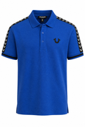 A royal blue short-sleeve polo shirt by True Religion, featuring black embroidered trim along the shoulders and sleeves with small white logo details, and a black embroidered crescent moon logo on the left chest.