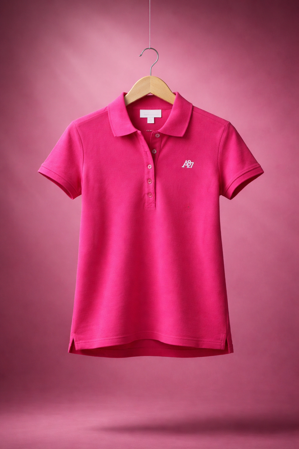 Pink polo shirt on a hanger against a pink background