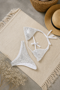 Beige woven mat with a white beaded bikini set and straw hat on a neutral background