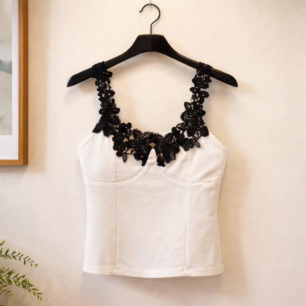 White top with black lace details on a hanger against a beige wall.