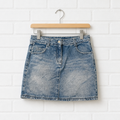 Blue denim skirt on a wooden hanger against a white brick wall.