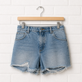 Blue denim shorts on a wooden hanger against a white brick wall.