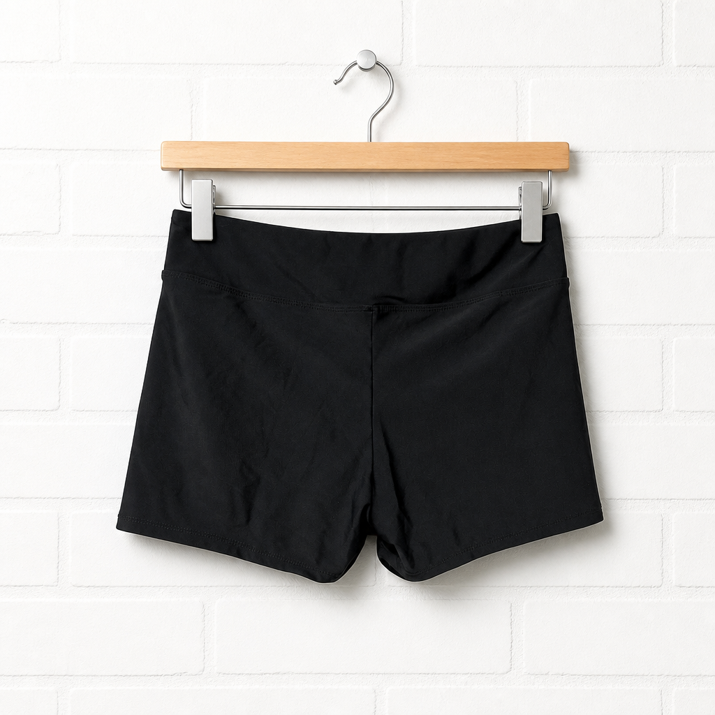 Black shorts hanging on a wooden hanger against a white tiled wall.
